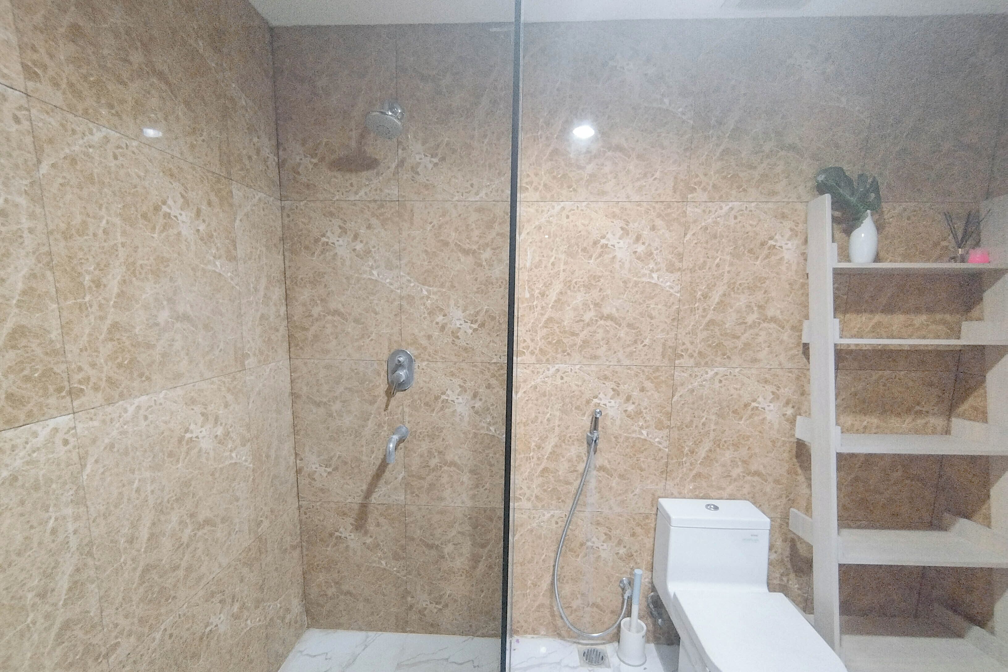 A bathroom with a glass shower enclosure, marble tiles, a white sink, and a shelf with a plant.