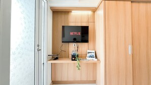 A room with a wooden cabinet, a television mounted on the wall, and a small shelf with a plant and a framed picture.