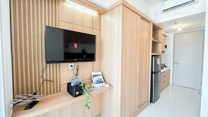 A modern kitchen with wooden cabinetry, a built-in TV, a refrigerator, and a countertop with a plant and travel brochures.