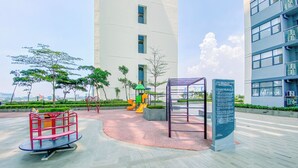 Un parque infantil con toboganes y estructuras para escalar, rodeado de una zona pavimentada con bancos y un cartel.
