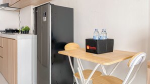 Cocina compacta con refrigerador, una mesita con cajas de botellas de agua y alacenas de madera.