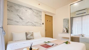 Ett hotellrum med en stor säng, ett sänggavel i marmor, ett nattduksbord med en bricka, en spegel och en luftkonditioneringsanläggning.