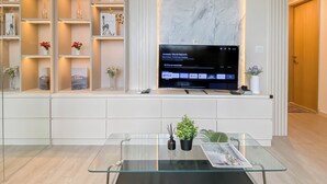 Ett modernt vardagsrum med en stor, platt-TV som är monterad på en vit vägg, omgivet av hyllor med dekorativa föremål och växter.