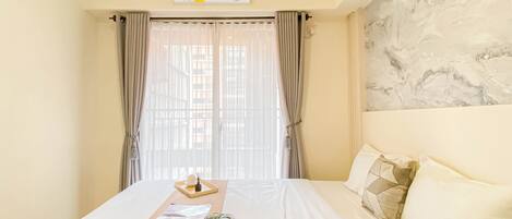 A hotel room with a bed, a bedside table with a tray, and a wall-mounted air conditioner.
