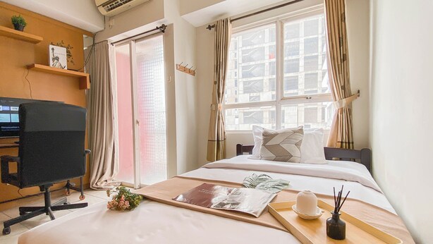 A hotel room with a bed, a desk, and a window with curtains. - Nice & Cozy Studio Apartment At Taman Melati Margonda (Depok)