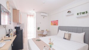 Makuuhuoneessa on sänky, yöpöytä ja työpöytä tuolilla. Huoneessa on ikkuna, jossa on verhot, ilmastointilaite ja seinälle kiinnitetty hylly, jossa on koristeena teksti ”HOME”.
