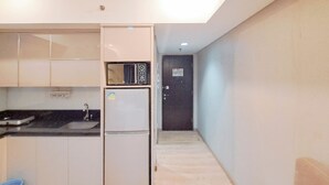 Eine kleine Küche mit Spüle, Kühlschrank und Mikrowelle. Eine Tür führt in einen weiteren Raum.