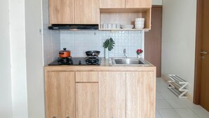 A compact kitchen with wooden cabinets, a gas stove, a sink, and a small countertop. - Simple Look 2Br At Apartment Podomoro Golf View (Gunung Putri)