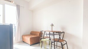 A small, bright room with a sofa, a small table with chairs, and a window with curtains. - Simple Look 2Br At Apartment Podomoro Golf View (Gunung Putri)