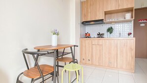 A small kitchen with wooden cabinets, a white tiled backsplash, and a small dining table with two chairs. - Simple Look 2Br At Apartment Podomoro Golf View (Gunung Putri)