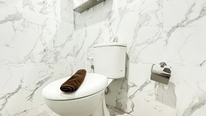 Une salle de bain avec des toilettes, des murs en marbre et une serviette posée sur la lunette.
