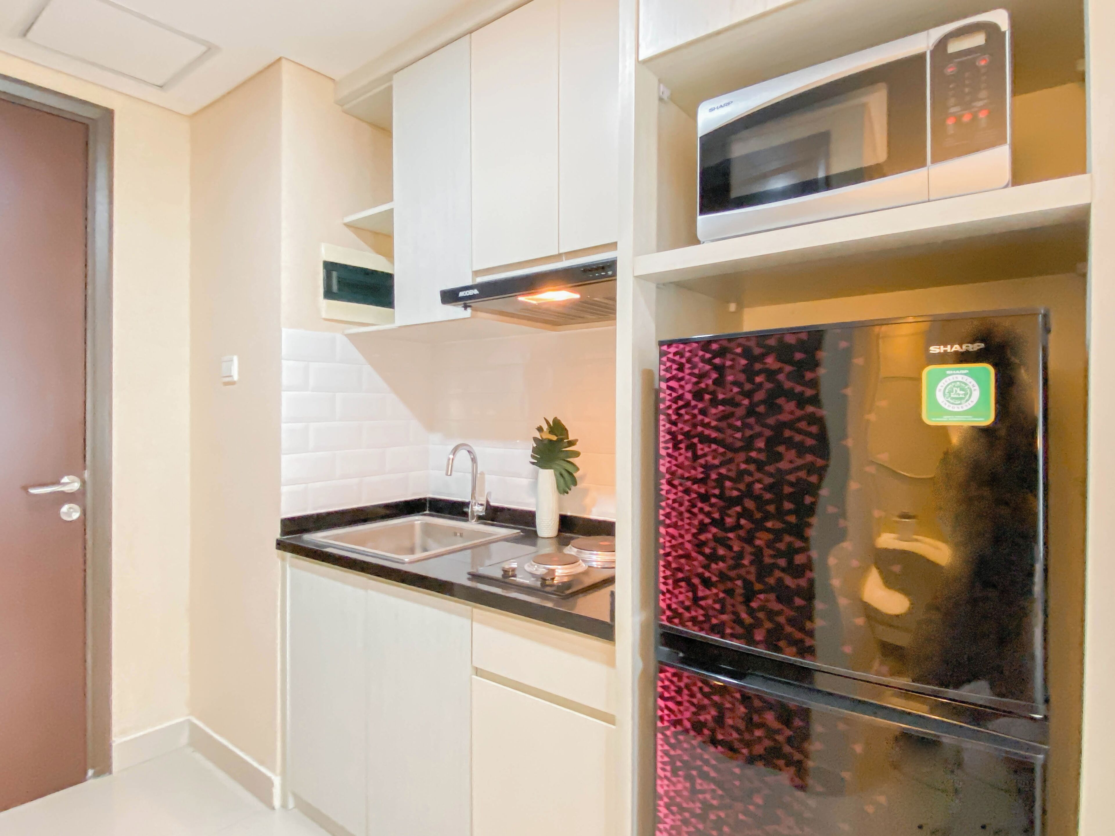 Een moderne keuken met witte kastjes, een roestvrijstalen spoelbak, een magnetron en een koelkast met een deur met een patroon.