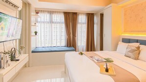 A hotel room with a bed, bedside table, TV, and a window with curtains. - Cream Toned And Compact Studio Apartment Pollux Chadstone (Cikarang)