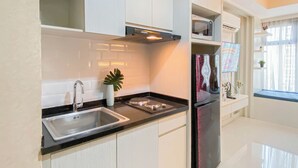 A modern kitchen with white cabinets, a stainless steel sink, a microwave, and a refrigerator. - Cream Toned And Compact Studio Apartment Pollux Chadstone (Cikarang)