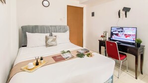 Ein Hotelzimmer mit einem Bett, einem Schreibtisch mit Fernseher, einem Sessel und einem kleinen Tisch mit Tablett.