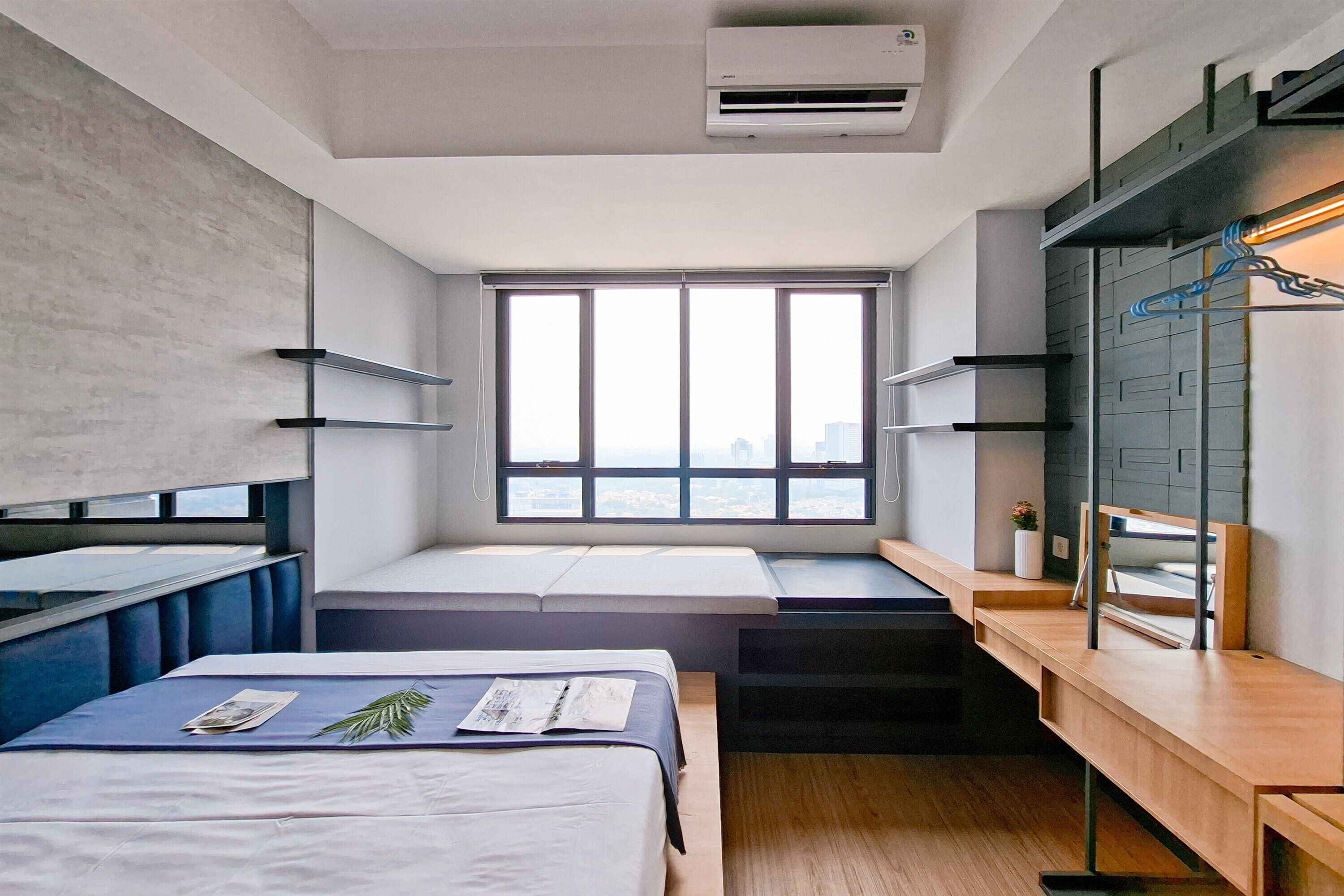 Quarto de hotel moderno com cama, escrivaninha, um banco e uma grande janela com vista para a cidade.