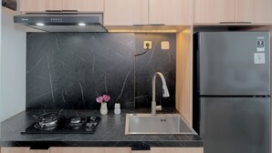 A modern kitchen with a black marble backsplash, stainless steel appliances, and wooden cabinets. - Minimalist Studio At Apartment Lrt City Bekasi (Bekasi)