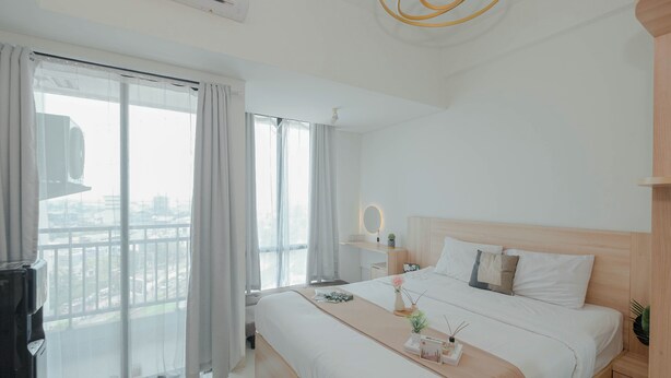 A modern hotel room with a large bed, a bedside table, a small desk, and a view of the city through large windows. - Minimalist Studio At Apartment Lrt City Bekasi (Bekasi)