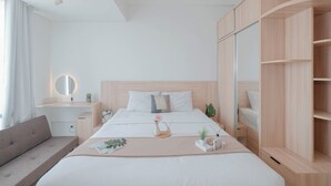A modern hotel room with a large bed, a bedside table with a mirror, a small plant, and a wooden wardrobe. - Minimalist Studio At Apartment Lrt City Bekasi (Bekasi)