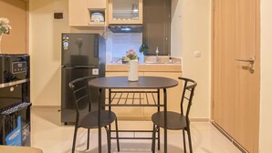 A compact kitchen with a refrigerator, a sink, and a dining area with two chairs and a table. - Warm Neutral 2Br At Meikarta Apartment (Cikarang)