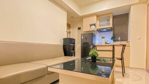 A modern kitchen with a built-in refrigerator, a coffee machine, and a small dining area with a glass table and a single chair. - Warm Neutral 2Br At Meikarta Apartment (Cikarang)