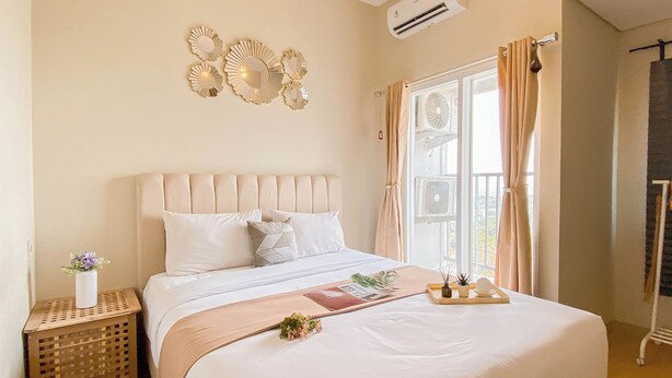 Une chambre avec un grand lit, une table de chevet avec une lampe, un climatiseur fixé au mur et une fenêtre avec des rideaux.