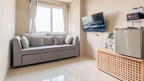 Un salon moderne avec un canapé gris, un téléviseur à écran plat fixé au mur, un réfrigérateur GE et une petite table en bois sur laquelle est posée une plante.