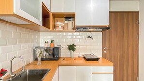 Une cuisine compacte avec des meubles blancs, un évier en acier inoxydable, un four à micro-ondes et un petit espace de comptoir agrémenté d’une plante et d’objets décoratifs.
