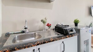 A kitchen with a stainless steel sink, a coffee machine, a small potted plant, and a speaker. - Neutral Minimalist Studio Apartment At Lrt City Sentul - Royal Sentul Park (Bogor)