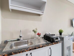 A kitchen with a stainless steel sink, a coffee machine, a small potted plant, and a speaker. - Neutral Minimalist Studio Apartment At Lrt City Sentul - Royal Sentul Park (Bogor)