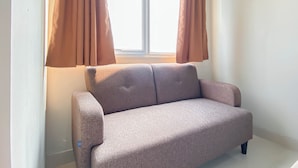 A room with a beige sofa, a window with brown curtains, and white walls. - Neutral Minimalist Studio Apartment At Lrt City Sentul - Royal Sentul Park (Bogor)