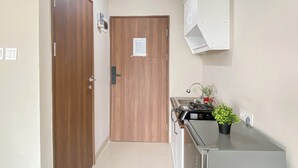 A hallway with a wooden door, a white cabinet, a sink with a faucet, and a potted plant. - Neutral Minimalist Studio Apartment At Lrt City Sentul - Royal Sentul Park (Bogor)