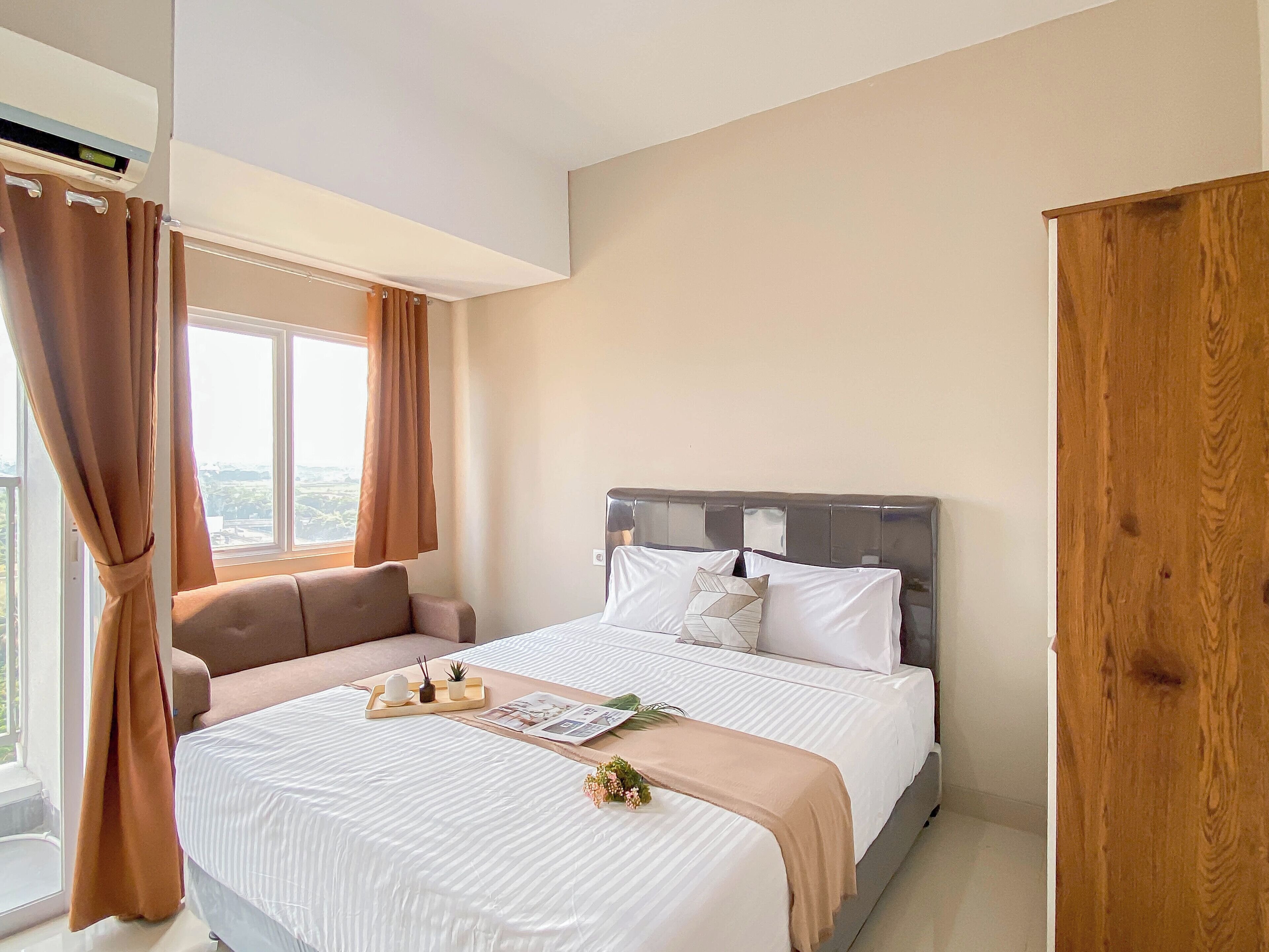 Een slaapkamer met een bed, een raam met gordijnen, een nachtkastje met dienblad, en een houten garderobe.