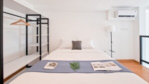 A modern hotel room with a bed, a wardrobe with shelves, a bedside table, a lamp, and an air conditioning unit. - Studio Loft Apartment Near Living World Alam Sutera At Kingland Avenue (South Tangerang)