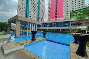 A swimming pool area with tiled flooring, black planters, and a covered seating area. - Soft And Strategic Studio At Green Pramuka City Apartment (Jakarta)