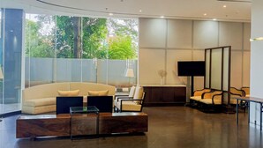 A modern lobby with a sofa, chairs, a coffee table, and a TV. - Good Deal Studio At Apartment Tamansari Bintaro Mansion (South Tangerang)