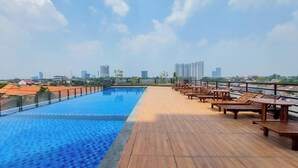A rooftop pool with a wooden deck and lounge chairs, overlooking a cityscape. - Good Deal Studio At Apartment Tamansari Bintaro Mansion (South Tangerang)