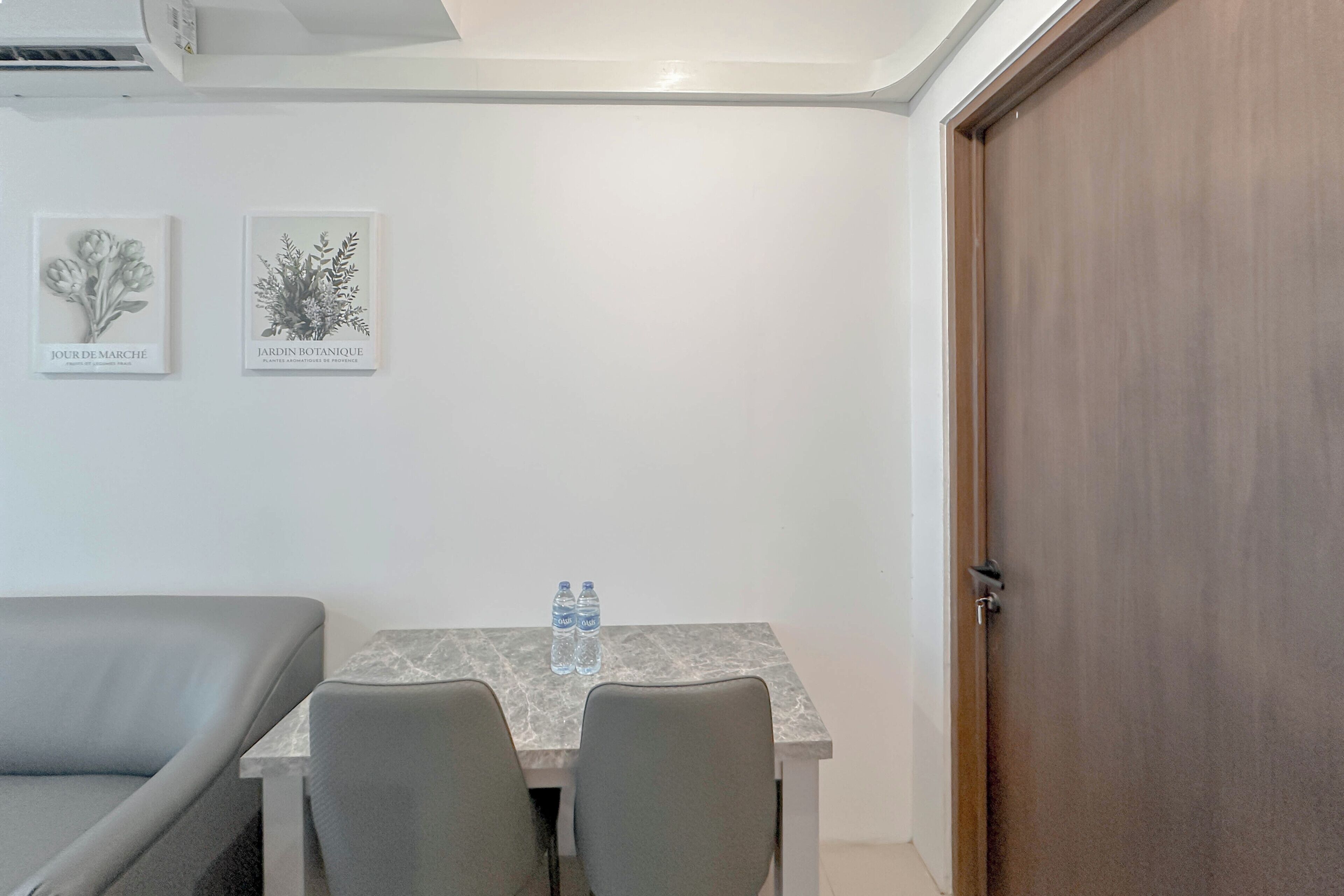 A room with a bed, a table with two chairs, two water bottles, and two framed botanical prints on the wall.