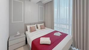 Una camera d'albergo moderna con un letto grande, un comodino e vista sulla città attraverso tende leggere.