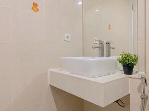 A bathroom with a white sink, a mirror, and a potted plant. - Basic Studio At Daan Mogot City Apartment (Jakarta)