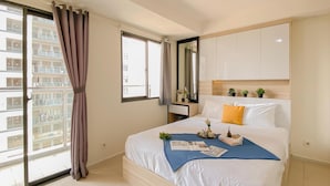 A modern hotel room with a large bed, a bedside table, a mirror, and a view of a building through the window. - Basic Studio At Daan Mogot City Apartment (Jakarta)