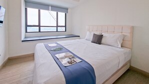 A neatly made bed with a headboard, a window with a view, and a small bench under the window. - Minimalist And Homey Studio At Apartment Collins Boulevard (Tangerang)