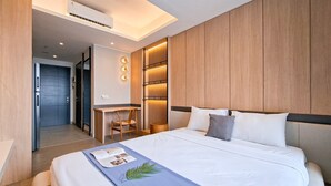 A modern hotel room with a large bed, a desk, and a seating area. - Cozy Warm Studio Apartment At Collins Boulevard (Tangerang)