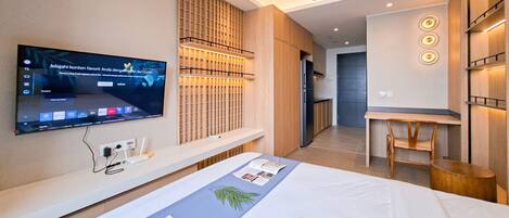A modern hotel room with a large bed, a TV mounted on the wall, a wooden partition, and a small desk area.
