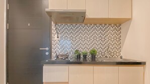 A compact kitchen with a black door, a tiled backsplash, and a black countertop. - Comfortable 1Br At Belmont Residence Puri Apartment (Jakarta)