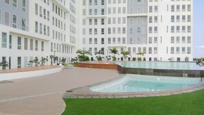 A modern hotel with a large pool area, surrounded by a well-maintained lawn and palm trees. - Basic Look Studio Near Bekasi Station At Patraland Urbano Apartment (Bekasi)