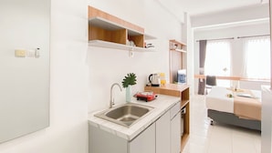A compact kitchen with a sink, countertop, and wooden shelves. - Basic Look Studio Near Bekasi Station At Patraland Urbano Apartment (Bekasi)