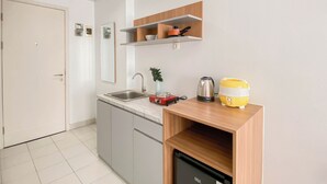 A compact kitchen with a sink, a coffee maker, and a yellow container on a wooden shelf. - Basic Look Studio Near Bekasi Station At Patraland Urbano Apartment (Bekasi)