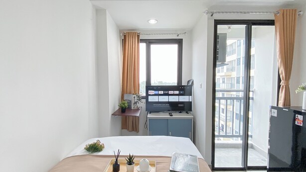 A hotel room with a bed, a desk with a computer, a window with curtains, and a view of the city. - Studio Apartment Jkt Living Star Near Citimall Cimanggis (Jakarta)