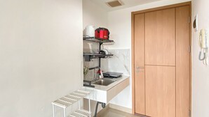 A compact kitchen with a sink, a stove, and a wooden door. - Studio Apartment Jkt Living Star Near Citimall Cimanggis (Jakarta)